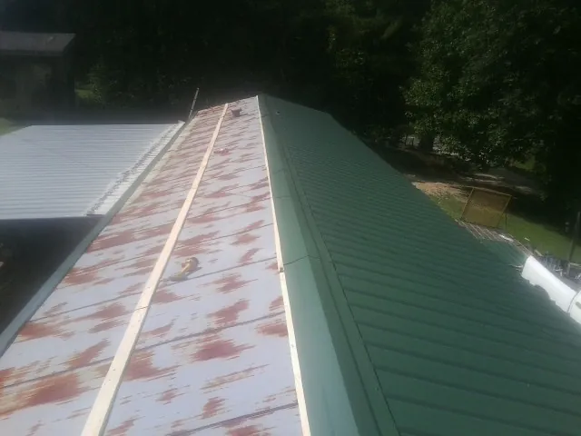 Old rusted panels beside newly installed green metal roofing — Wind Damage Roof Repair by Roofing Brothers in Patton