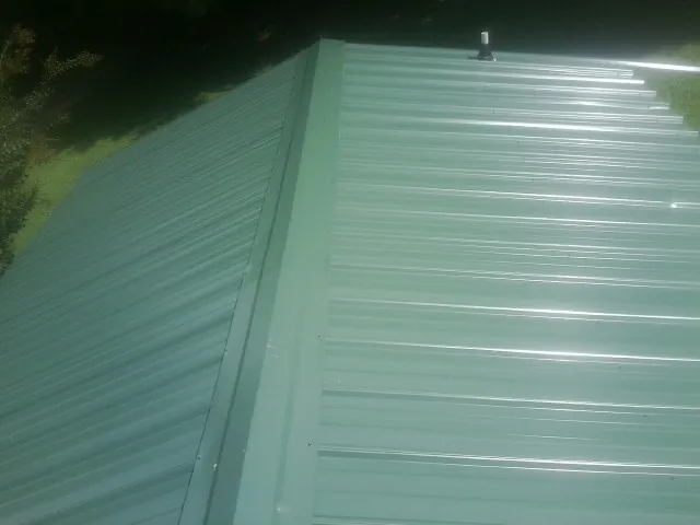 New green metal panels meeting at the ridge of a roof — Flat Roof Repair work by our crew in Patton