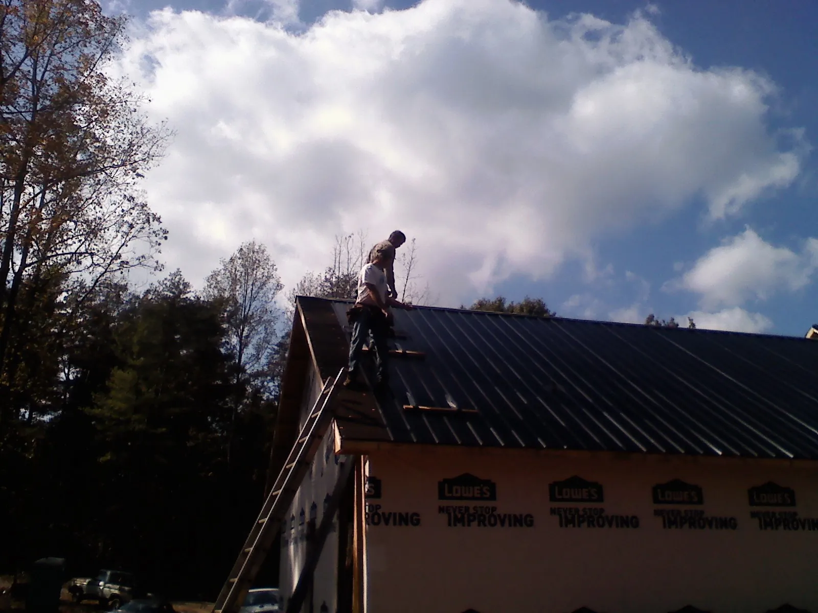 Roofer fastening dark metal panels high against a cloudy sky, from a Roof Inspection job in Patton